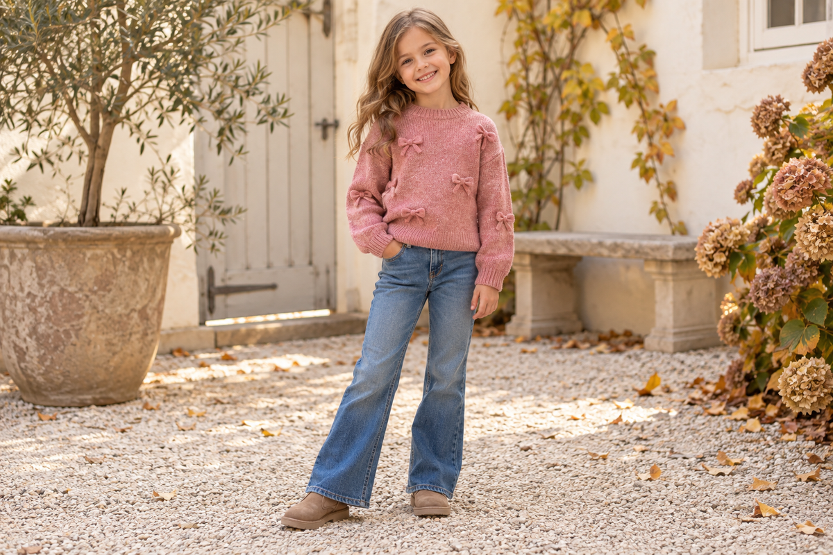 Meisje in een roze gebreide trui met strikjes en een flared jeans